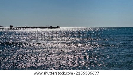 Wooden bridge to the sea Glare on the blue sea water. Sandy beach 
