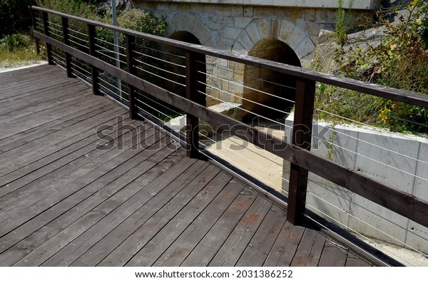 wooden bridge with a stone\
foundation newly built for cyclists over a stream by the pond.\
wooden beams connected by screws and rope stainless steel cable\
railings