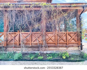 A wooden cabin porch with vine-covered walls and bed of spring flowers in front - Powered by Shutterstock