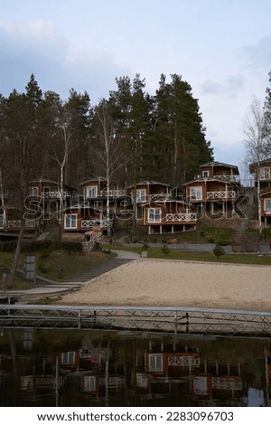 Wooden camp by the lake, small cottages in the woods between high trees in early spring, cozy beach