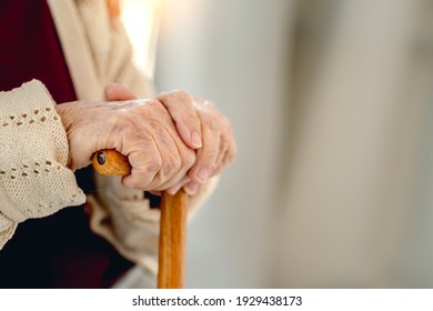 Wooden cane in hand of old woman sitting in light room