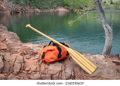 wooden canoe paddle and waterproof duffel on a rocky shore of mountain lake - Horsetooth Reservoir in northern Colorado