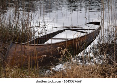 A Wooden Canoe Sinking And Filled With Water At A Lake Shore