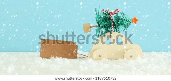 Wooden car carrying a christmas tree in front\
of blue background