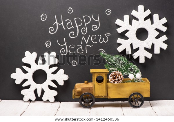 Wooden car with a\
Christmas branch in the back and foam snowflakes on the background\
of chalk black board