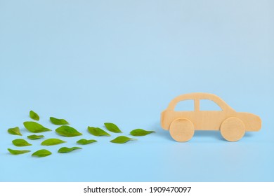 Wooden Car Model Emitting Fresh Green Leaves On Blue Background. Sustainable, Clean And Green Energy And Biofuel And Biodiesel For Transportation Industry Concept.