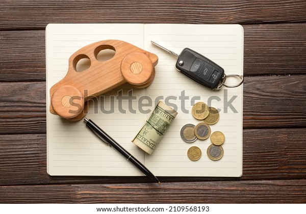 Wooden car with money, key and notebook on\
dark wooden background
