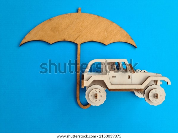 Wooden car under umbrella protection\
and transport insurance. Security car insurance\
concept