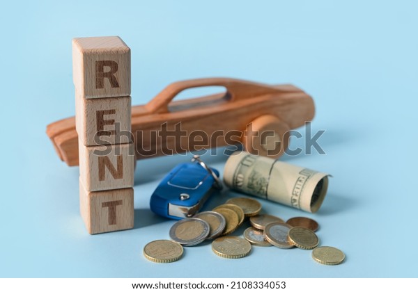 Wooden car with word RENT, key and money on\
blue background