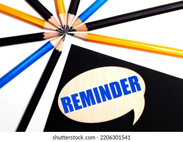 Wooden Card With The Text REMINDER On A Black Background Near Multicolored Pencils.