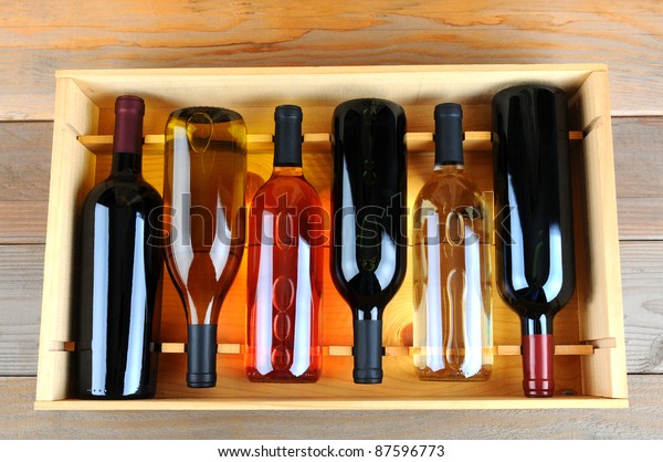A wooden\
case of assorted wine bottles without labels on a wood plank winery\
floor. Horizontal format overhead\
view.