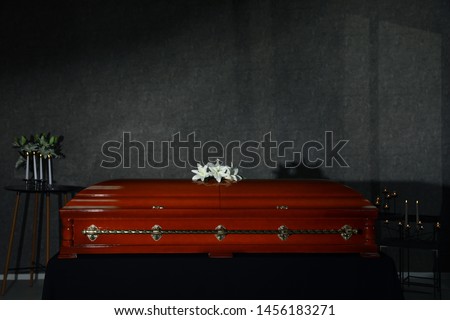 Wooden casket with white lilies and burning candles in funeral home