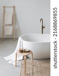 Wooden chair with soap bar and natural cosmetics for spa procedure close to tub. Vertical shot of white classic bathtub and home decor in modern interior. Comfortable bathroom in hotel