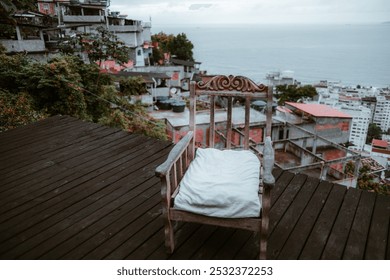 Wooden chair with white cushion on a dark wooden deck overlooking a vibrant favela hillside and ocean view. The rustic urban setting contrasts with natural greenery and blue waters - Powered by Shutterstock