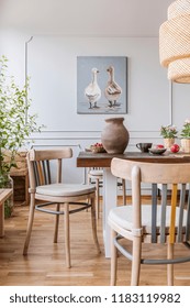 Wooden chairs at table in natural white dining room interior with poster and lamp. Real photo