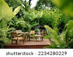 Wooden chairs and tables on the street in the tropics among the foliage. Exterior of cafe or lounge zone.