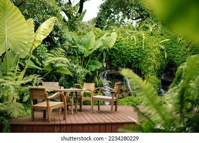 Wooden chairs and tables on the street in the tropics among the foliage. Exterior of cafe or lounge zone.