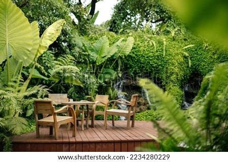 Wooden chairs and tables on the street in the tropics among the foliage. Exterior of cafe or lounge zone.