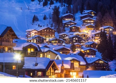 Wooden chalets covered with deep snow in cold winter season at the blue hours in Alps mountain region