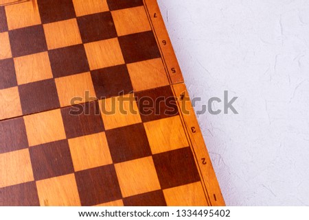 Wooden chess board, cropped image. Empty chess board on light background.