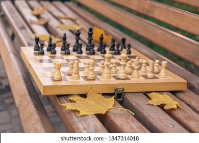 Wooden Chessboard With Pieces On A Bench In The Autumn City Park. Shallow Depth Of Field. Focus On The White Pieces.