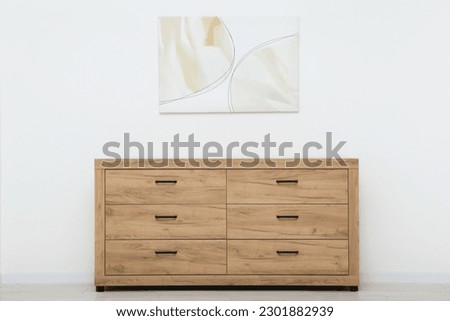Wooden chest of drawers and beautiful picture on white wall indoors. Interior design