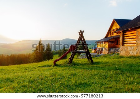 wooden children playground in highland landscape and small cottage..
