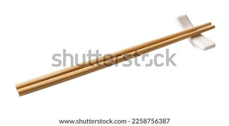 Wooden chopsticks on a white chopstick rest cutout. Pair of bamboo chopsticks on a porcelain holder  isolated on a white background. Japanese, Chinese, East Asian tableware concept. Top view.