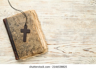 Wooden Christian cross and old Bible on white table, top view. Space for text