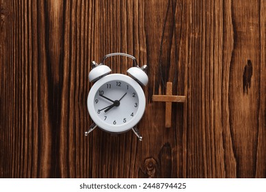 Wooden Christian cross on a string and alarm clock, wooden table. Prayer time