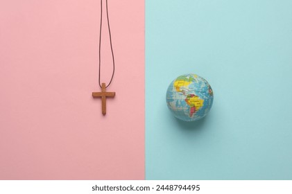 Wooden Christian cross on a string with globe on pink blue background. Messianism, Christian religion