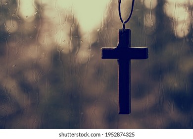 Wooden Christian Cross Pendant In Front Of Rain Drenched Window