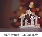 A wooden Christmas Nativity set with the holy family gazing at baby Jesus with a bokeh background.