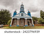 Wooden church Nuestra Senora Del Patrocinio in Tenaun on Chiloe with a white facade, blue stars and steeples and white columns in the entrance area.