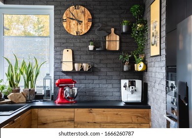 Wooden clock on black brick wall in trendy kitchen with red kitchen robot