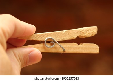 Wooden clothespin with fingers holding on dark background.