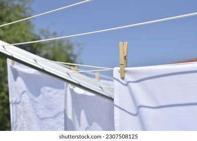 A wooden clothespin holds white laundry on a clothesline outdoors.