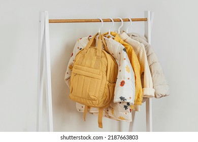 Wooden Clothing Rack With Children's Autumn Outfit. Yellow Backpack,  Jacket And Sweaters On Hangers In Wardrobe. Nursery Storage Ideas. Home Kids Wardrobe. 