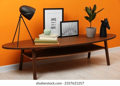 Wooden coffee table with different decor near orange wall indoors. Stylish interior design - Powered by Shutterstock