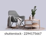 Wooden coffee table with houseplant and vase near cozy rocking chair on grey background