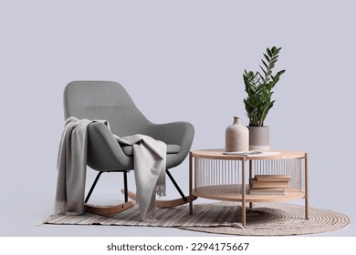 Wooden coffee table with houseplant and vase near cozy rocking chair on grey background