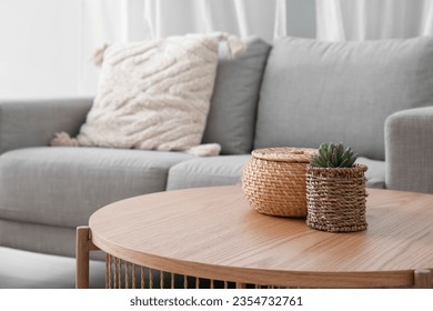 Wooden coffee table with with houseplant and wicker basket near grey sofa in living room - Shutterstock ID 2354732761
