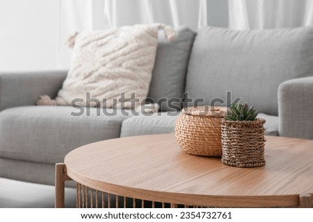 Wooden coffee table with with houseplant and wicker basket near grey sofa in living room
