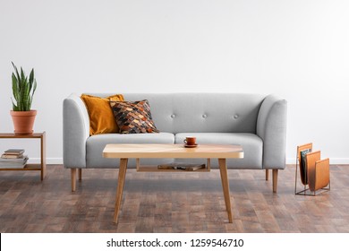 Wooden Coffee Table In The Middle Of Elegant Living Room With Grey Couch And Magazine Rack On The Wooden Floor, Real Photo