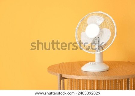 Wooden coffee table with modern electric fan near orange wall