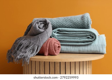 Wooden coffee table with stack of soft blankets on orange background