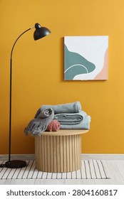 Wooden coffee table with stack of soft blankets near orange wall