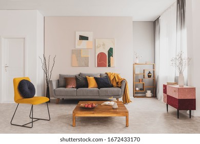 Wooden Coffee Table And Yellow Chair In Front Of Grey Couch With Pillows In Trendy Living Room