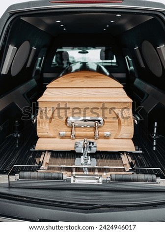 A wooden coffin stands in a black hearse. A simple wooden coffin in a black car. Funeral and farewell ceremony. Close-up photo.