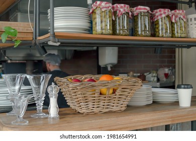 A wooden counter with a basket of fruit and plates, a shelf with glass jars of olives in the restaurant. - Powered by Shutterstock